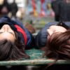 two women laying on a bench with their heads on each other