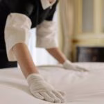 A housekeeper straightening the bed linens in a well-appointed hotel room.
