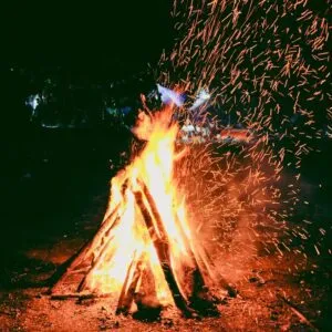 High flames and sparks fly from a vibrant outdoor campfire at night, creating a warm and lively scene.