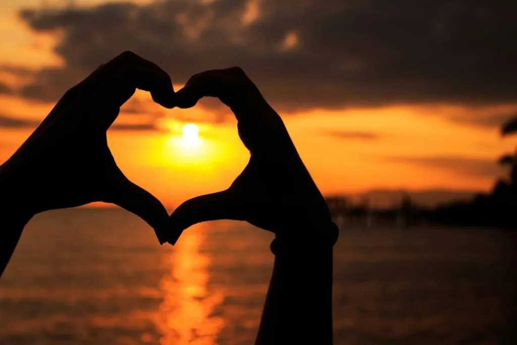 Silhouette of hands forming a heart against a beautiful seaside sunset.