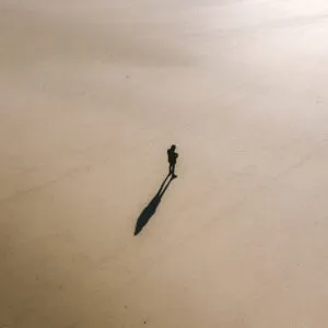 From above of unrecognizable person standing on smooth sandy ground and shadow behind