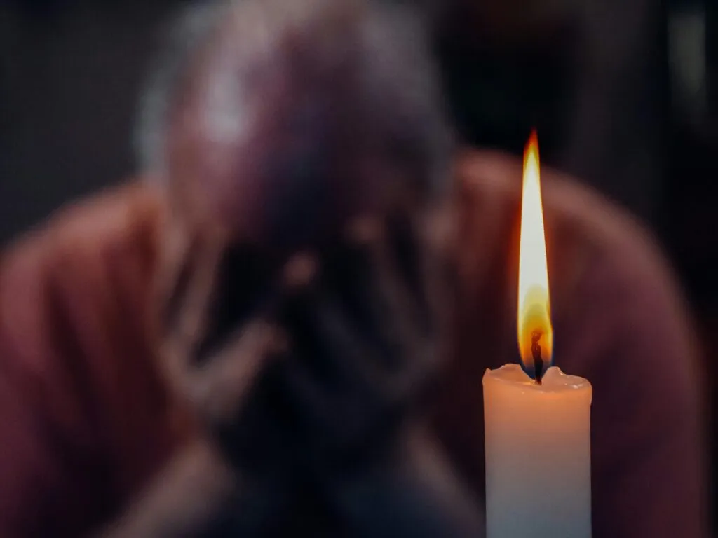 A senior adult in an emotional moment lit by a candle, symbolizing reflection and grief.