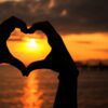 Silhouette of hands forming a heart against a beautiful seaside sunset.