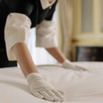 A housekeeper straightening the bed linens in a well-appointed hotel room.
